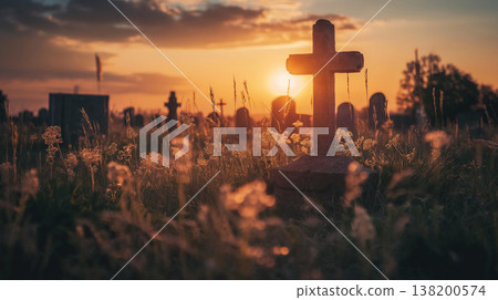 Peaceful cemetery scene at sunset, featuring a stone cross surrounded by wild grass, with the sun setting beautifully in the background and other tombstones visible. 138200574