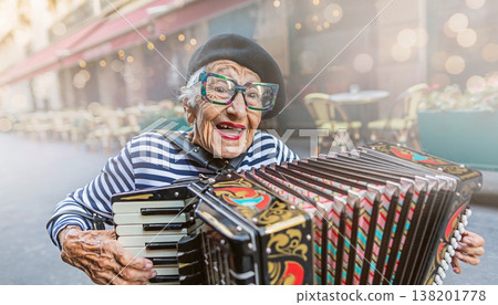 Elderly woman plays accordion on street with chairs and tables in background at an outdoor cafe in daytime 138201778
