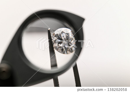 Diamond viewed through a magnifying glass held by tweezers Diamond viewed through a magnifying glass held by tweezers 138202058