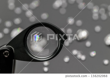 Magnifying glass highlights detailed facets of diamond-like stones against soft Magnifying glass highlights detailed facets of diamond-like stones against soft 138202068