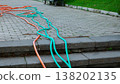 Long turquoise and orange garden hoses sprawled across a stone tile path next to a green lawn 138202135