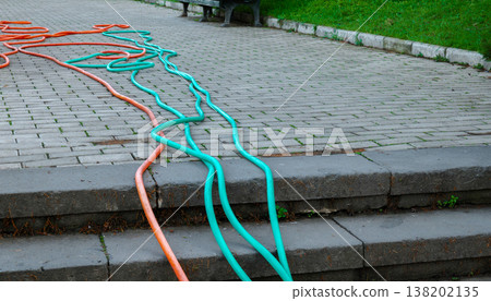 Long turquoise and orange garden hoses sprawled across a stone tile path next to a green lawn Long turquoise and orange garden hoses sprawled across a stone tile path next to a green lawn 138202135