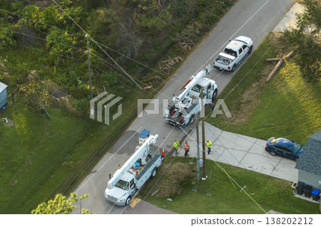 Electrician workers repairing damaged power lines using bucket trucks after hurricane Ian in Florida residential area Electrician workers repairing damaged power lines using bucket trucks after hurricane Ian in Florida residential area 138202212