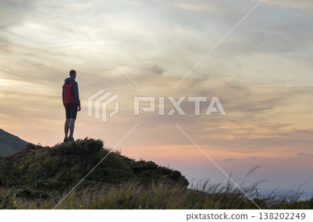 Dark silhouette of a hiker on a mountain at sunset standing on summit like a winner. Dark silhouette of a hiker on a mountain at sunset standing on summit like a winner. 138202249