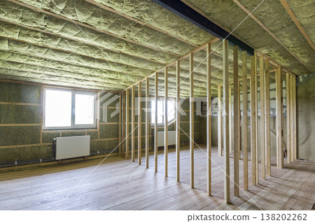 Construction and renovation of big light spacious empty room with oak floor, walls and ceiling insulated with rock wool, heating radiators under low attic windows and wooden frame for future walls. 138202262