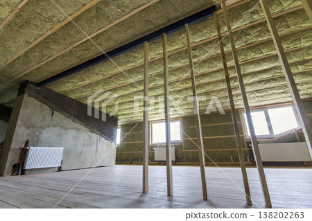 Construction and renovation of big light spacious empty room with oak floor, walls and ceiling insulated with rock wool, heating radiators under low attic windows and wooden frame for future walls. 138202263