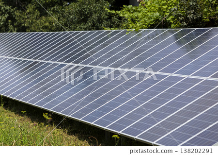 Close-up surface of lit by sun modern saving efficient stand -alone blue shiny solar photo voltaic panels system producing renewable clean energy on green grass and trees foliage background. 138202291