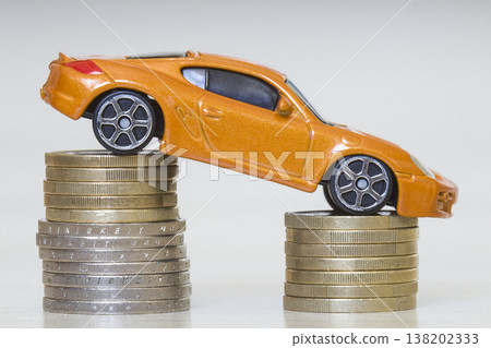 Close-up photo of new bright shiny yellow luxurious expensive toy sport car on two piles of metallic golden and silver coins as symbol of financial prosperity, wealth, vehicle sale and purchase. 138202333