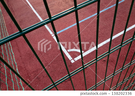 Close-up of white marking lines of outdoor basketball court fenced with protective metal fence. 138202336