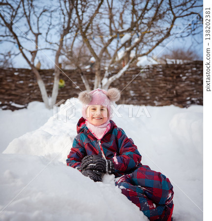 Smiling girl winter clothes holding large snowball standing in deep snow near house wooden fence Smiling girl winter clothes holding large snowball standing in deep snow near house wooden fence 138202381