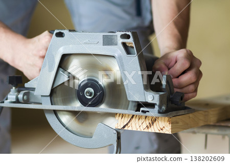 Close-up of muscular carpenter hands using new shiny modern powerful circular sharp electrical saw for cutting hard wooden board. Professional tools for construction and building concept. 138202609