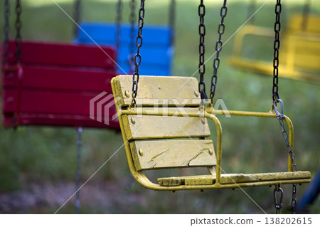 Close-up of empty wooden blue, yellow, vintage seats of multi-colored carousel hanging on chains. 138202615