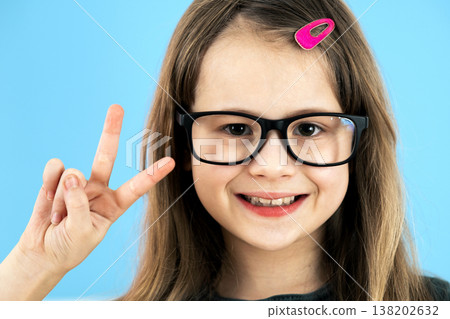 Close up portrait of a child school girl wearing looking glasses isolated on blue background. Close up portrait of a child school girl wearing looking glasses isolated on blue background. 138202632