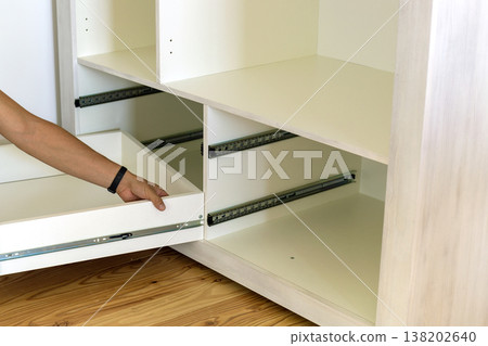 Close up of carpenter hands installing wooden drawer on sliding skids in contemporary cupboard cabinet. Close up of carpenter hands installing wooden drawer on sliding skids in contemporary cupboard cabinet. 138202640