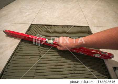 Ceramic tiles and tools for tiler. Worker hand installing floor tiles. Home improvement, renovation - ceramic tile floor adhesive, mortar, level. 138202646