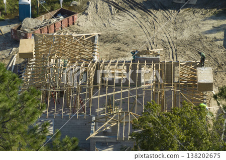 Builders working on roof construction of unfinished residential house with wooden frame structure in Florida suburban area. Housing development concept 138202675