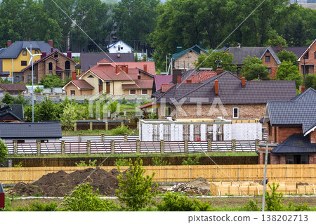 Beautiful view summer panorama of modern quiet suburban residential area. Nice comfortable two- storied new cottages with colorful tile roofs, yards and gardens on distant high buildings background. Beautiful view summer panorama of modern quiet suburban residential area. Nice comfortable two- storied new cottages with colorful tile roofs, yards and gardens on distant high buildings background. 138202713