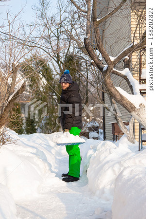 Man in winter jacket shoveling snow with shovel in front of brick house after heavy snowfall Man in winter jacket shoveling snow with shovel in front of brick house after heavy snowfall 138202822
