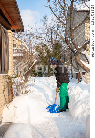 Man in winter jacket shoveling snow with shovel in front of brick house after heavy snowfall Man in winter jacket shoveling snow with shovel in front of brick house after heavy snowfall 138202824