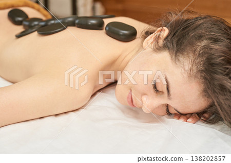 Young Caucasian Female Enjoying Relaxing Hot Stone Massage At Spa For Mindfulness And Serenity Young Caucasian Female Enjoying Relaxing Hot Stone Massage At Spa For Mindfulness And Serenity 138202857