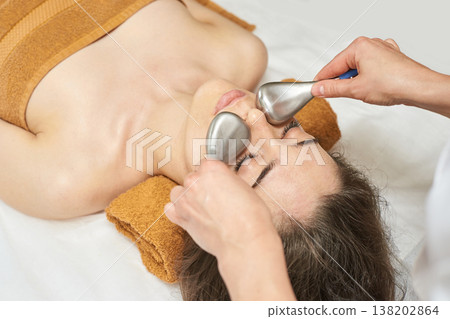 Young Caucasian Female Enjoying Relaxing Facial Massage Using Metal Tools In Spa Setting For Young Caucasian Female Enjoying Relaxing Facial Massage Using Metal Tools In Spa Setting For 138202864