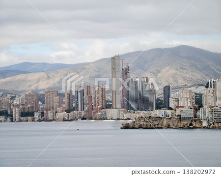 Urban highrise by mountains, Tall building overlooking sea with mountain scenery and tranquil water Urban highrise by mountains, Tall building overlooking sea with mountain scenery and tranquil water 138202972