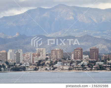 Energetic coastal neighborhood featuring midlevel towers and busy promenade with mountain landscape beyond 138202986