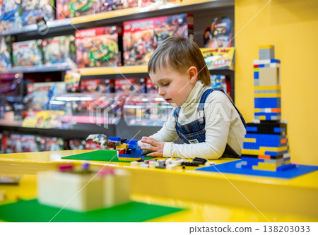 Little boy focused on assembling colorful building bricks bright table inside toy store environment Little boy focused on assembling colorful building bricks bright table inside toy store environment 138203033