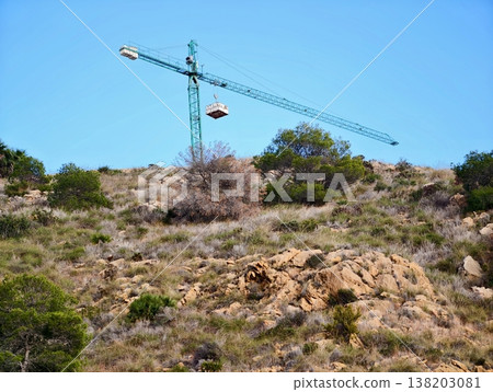 Gondola transports supplies, Aerial crane moves cargo across rocky hillside landscape under blue sky Gondola transports supplies, Aerial crane moves cargo across rocky hillside landscape under blue sky 138203081