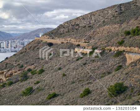 Trail overlooking skyline and coastal bay, Mountain route with distant cityscape and bay scenery surface 138203104