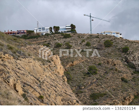 Industrial construction scene, Urban development activity against rugged hillside under cloudy sky Industrial construction scene, Urban development activity against rugged hillside under cloudy sky 138203134