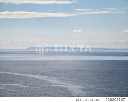 Serene scene depicting layered cloud formations over placid sea with subtle pastel hues and distant landmasses Serene scene depicting layered cloud formations over placid sea with subtle pastel hues and distant landmasses 138203167