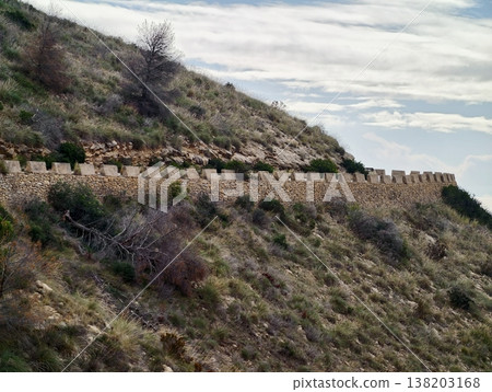 Path along high hillside with distant town, Elevated route tracing steep terrain beneath cloudy skies Path along high hillside with distant town, Elevated route tracing steep terrain beneath cloudy skies 138203168