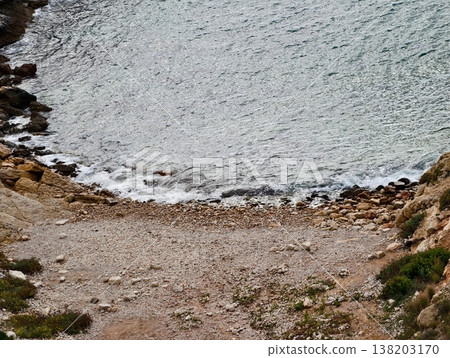 Calm peaceful shoreline with textured stones and sparse greenery ideal for relaxation and photography 138203170