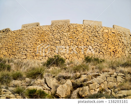 Sundrenched round stone wall with lush grass foreground showcasing weathered craftsmanship Sundrenched round stone wall with lush grass foreground showcasing weathered craftsmanship 138203181