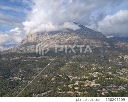 Majestic mountain shrouded in clouds overlooking peaceful farmland and winding country roads 138203209