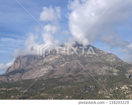 Rugged mountain summit under swirling weather, Dramatic rocky mountain peak shrouded in mist and shadows Rugged mountain summit under swirling weather, Dramatic rocky mountain peak shrouded in mist and shadows 138203229