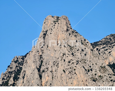 Sunlit rocks with dramatic features, Vertical limestone formation with sharp edges under clear sky scene 138203348