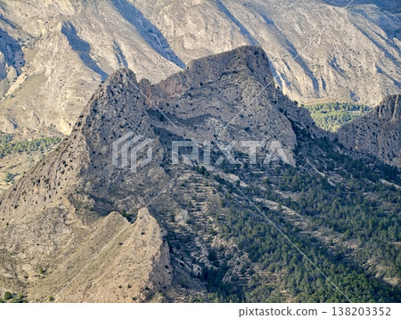 Rugged peak with scenic views, Jagged mountain rise highlighted by sunlight above verdant landscape 138203352