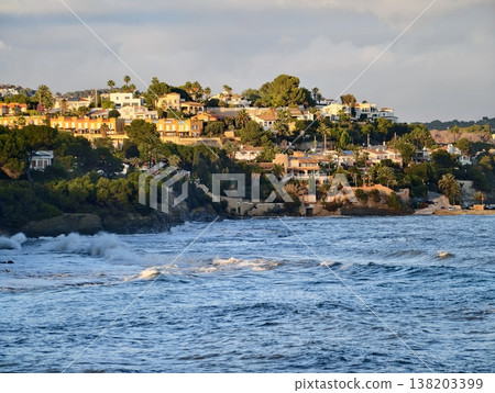 Lush cliffs with ocean views, Sunlit dwellings nestled among greenery overlooking lively rolling surf Lush cliffs with ocean views, Sunlit dwellings nestled among greenery overlooking lively rolling surf 138203399