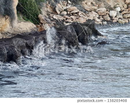 Crashing surf over rugged rocky shoreline, Wet stones and swirling tides under stormy cloudy sky 138203408