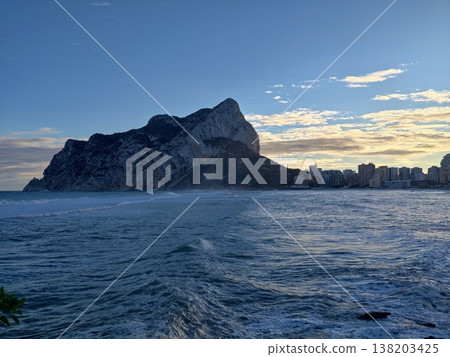 Monolith against sunset, Striking monolith rises from ocean as sunset bathes scene in gold light 138203425