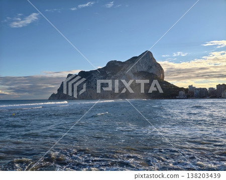 Bright coastal morning, Sunrise over rocky shoreline, Shimmering water against vibrant blue sky backdrop Bright coastal morning, Sunrise over rocky shoreline, Shimmering water against vibrant blue sky backdrop 138203439