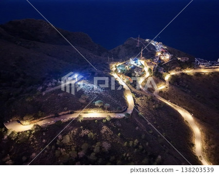 Nighttime mountain scene with illuminated path and distant electrical installations visible Nighttime mountain scene with illuminated path and distant electrical installations visible 138203539