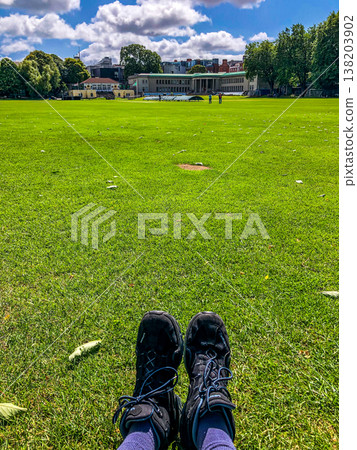 Individual with bare feet is standing on vibrant green grass, enjoying the warmth of sunlight, while wearing comfortable denim jeans, evoking a sense of relaxation and nature 138203902
