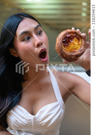 Surprised Young Thai Woman Holding Egg Tart in Hong Kong 138204615