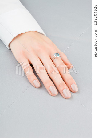 Beautiful female hand with gold ring with diamonds and aquamarine on gray background Beautiful female hand with gold ring with diamonds and aquamarine on gray background 138204926