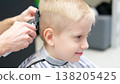 Child receiving a haircut from a hairdresser in barbershop 138205425