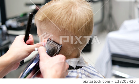 Child getting a haircut with clippers in a barbershop Child getting a haircut with clippers in a barbershop 138205426