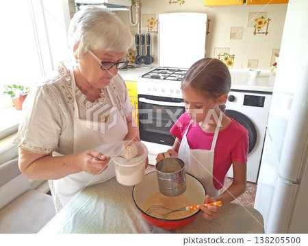 A grandmother and her granddaughter are making pancakes in the kitchen. A grandmother and her granddaughter are making pancakes in the kitchen. 138205500